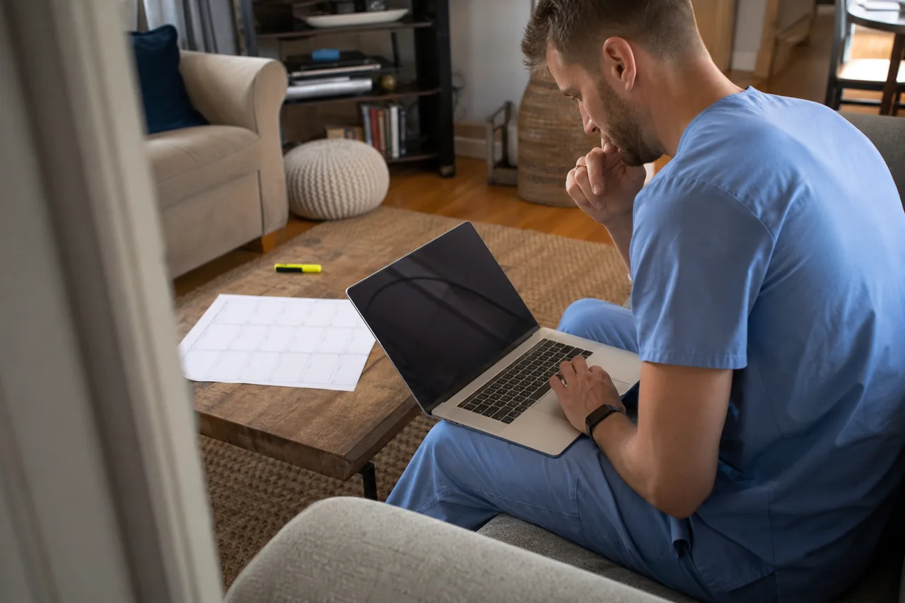 Physician assistant graduate on a couch comparing PANCE review courses on a laptop with an exam calendar on the table